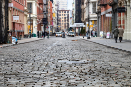 Cobblestone street with busy intersection blurred in the background in the SoHo neighborhood of New York City
