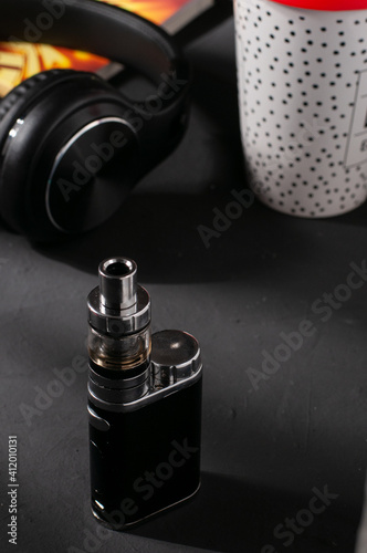 main shot of an electronic cigarette with headphones in the background and coffee cup and black background