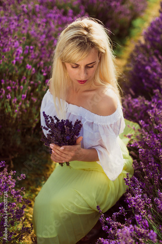 The beautiful young woman sitting in the lavender field and holding the bouquet of lavender in hands