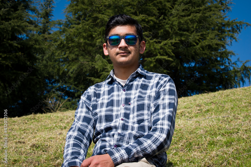 boy sitting in green grass field looking upward wearing t shirt and blue sunglasses boy sitting in green grass field looking upward wearing t shirt and blue sunglasses