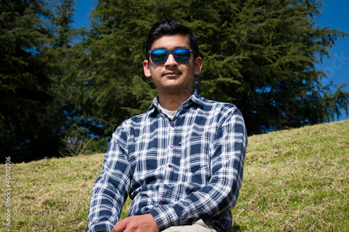 boy sitting in green grass field looking upward wearing t shirt and blue sunglasses