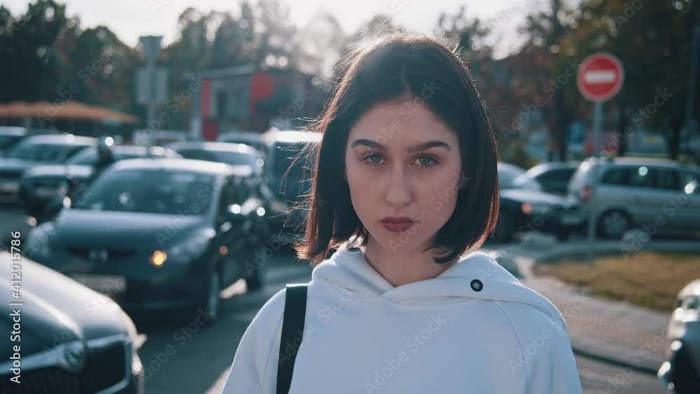 Short haired woman. Static camera view of brunette stylish attractive girl posing at the camera at the autumn street. Riding cars at the background. Subcultures, teenagers and fashion concept