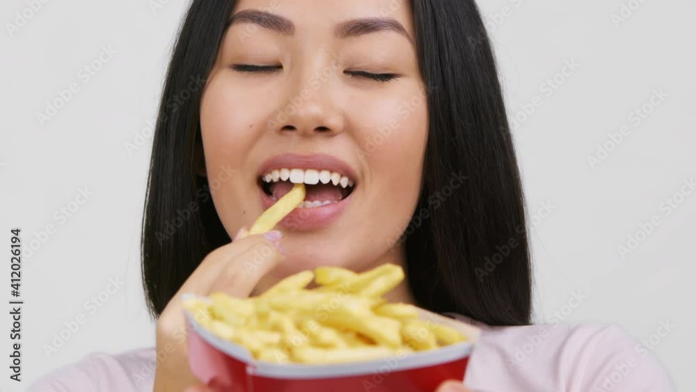 Asian Woman Eating French Fries Enjoying Junk Food, White Background Asian Woman Eating French Fries Enjoying Junk Food, White Background