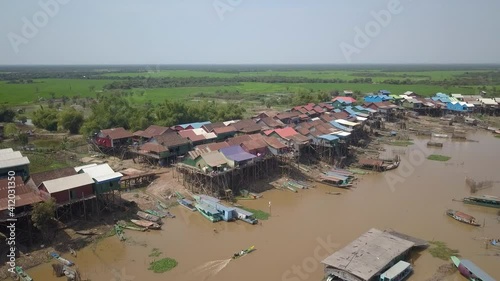 descending drone shot of a long tail fishing boat sailing through a floating village in the Tonle sap river during the dry season