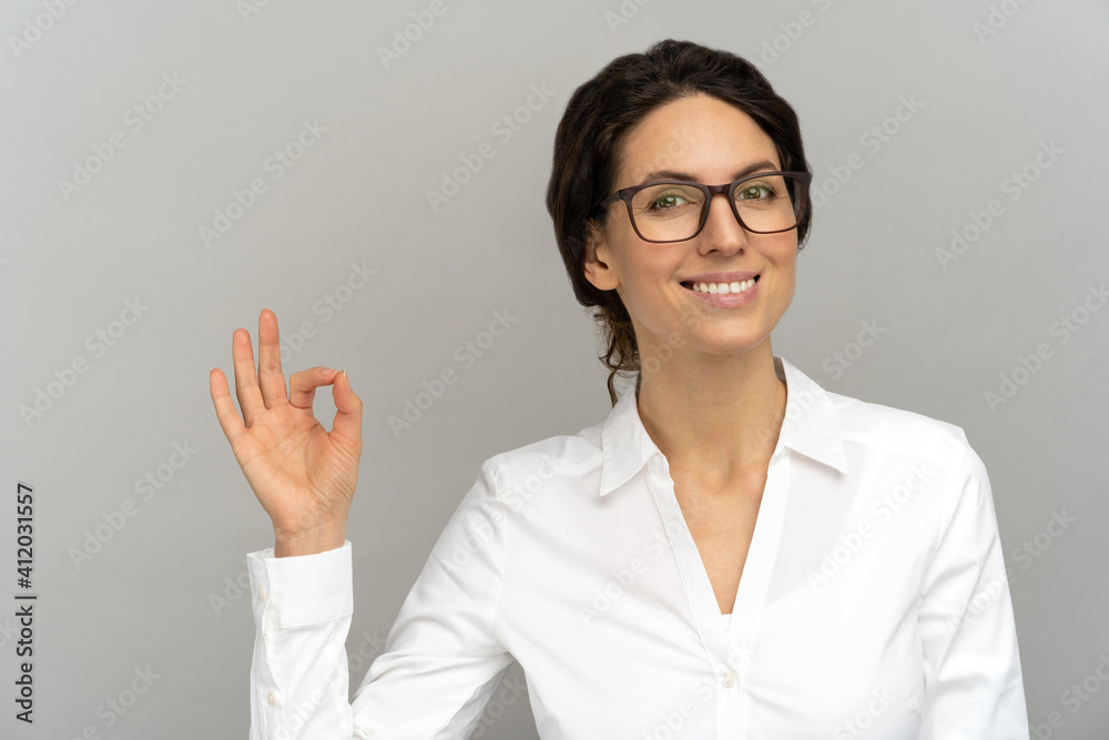 Cheerful business woman wear blouse in good mood smiling broadly, showing ok sign over studio grey background. Positive office employee female advertises a product. Customer, sale, discount. Cheerful business woman wear blouse in good mood smiling broadly, showing ok sign over studio grey background. Positive office employee female advertises a product. Customer, sale, discount.