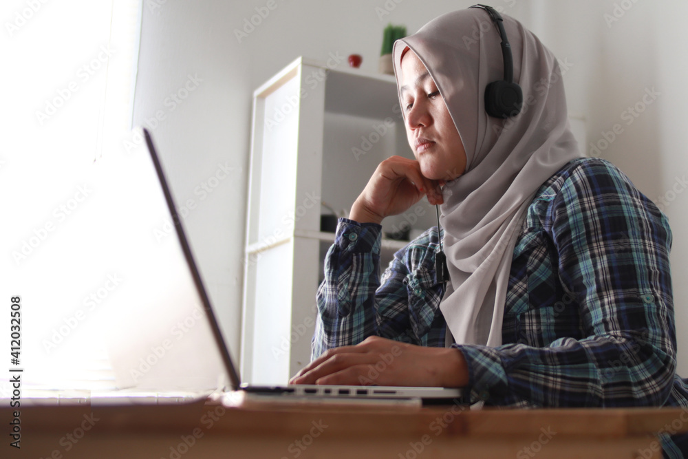Asian muslim woman having video teleconference on her laptop at home, online learning or working from home