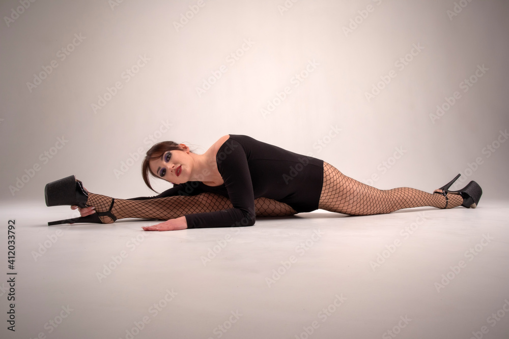 attractive brunette with braided hair in a black bodysuit and black high-heeled shoes in the studio on a light background