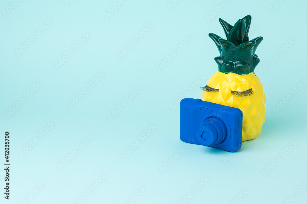 Fototapeta premium A yellow pineapple with a blue camera takes pictures of a pumpkin in a hat.