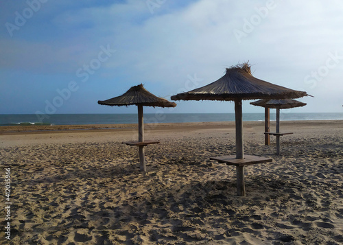 Sombrillas de paja en una playa vacía con el el mar calmo y el cielo celeste.