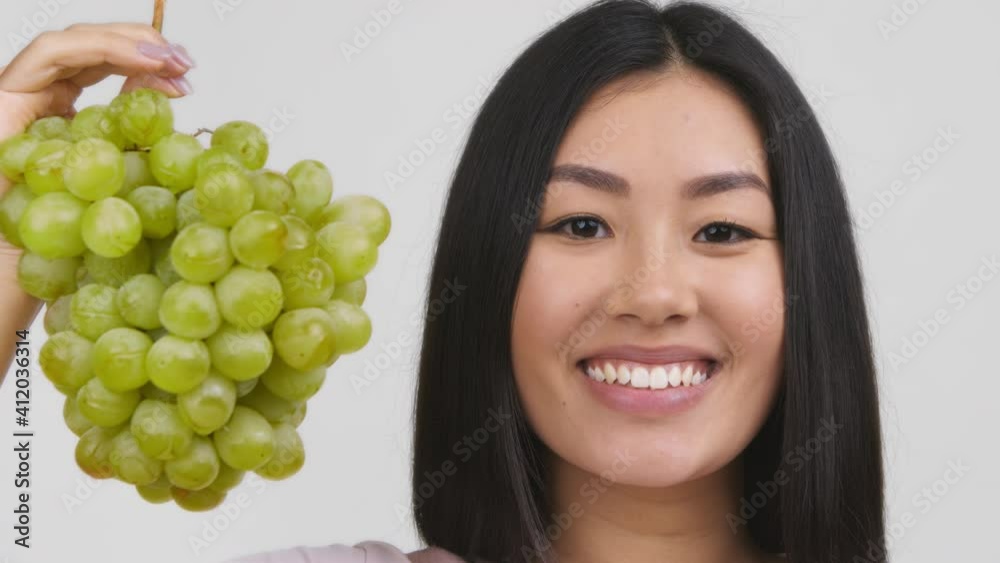 Asian Lady Holding Bunch Of Grapes Near Face, White Background Asian Lady Holding Bunch Of Grapes Near Face, White Background