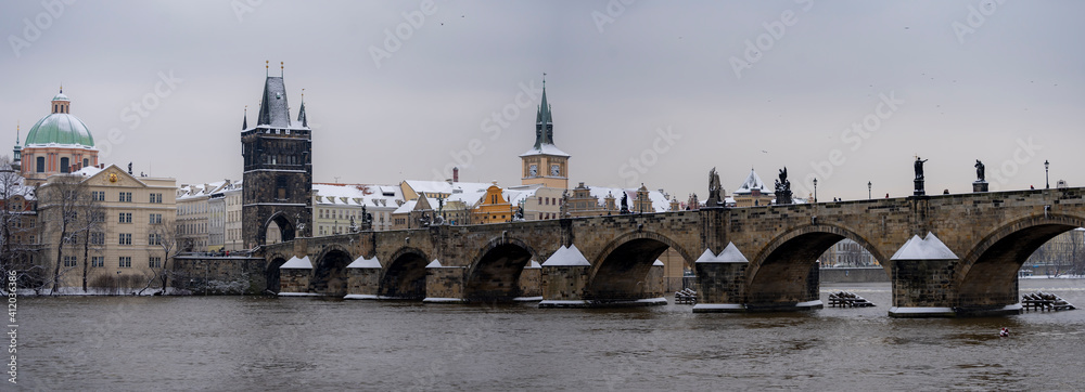 panoramic view of the snow-covered Charles Bridge on the Vltava River and snow on the roofs of buildings and towers in the center of the old town of Prague