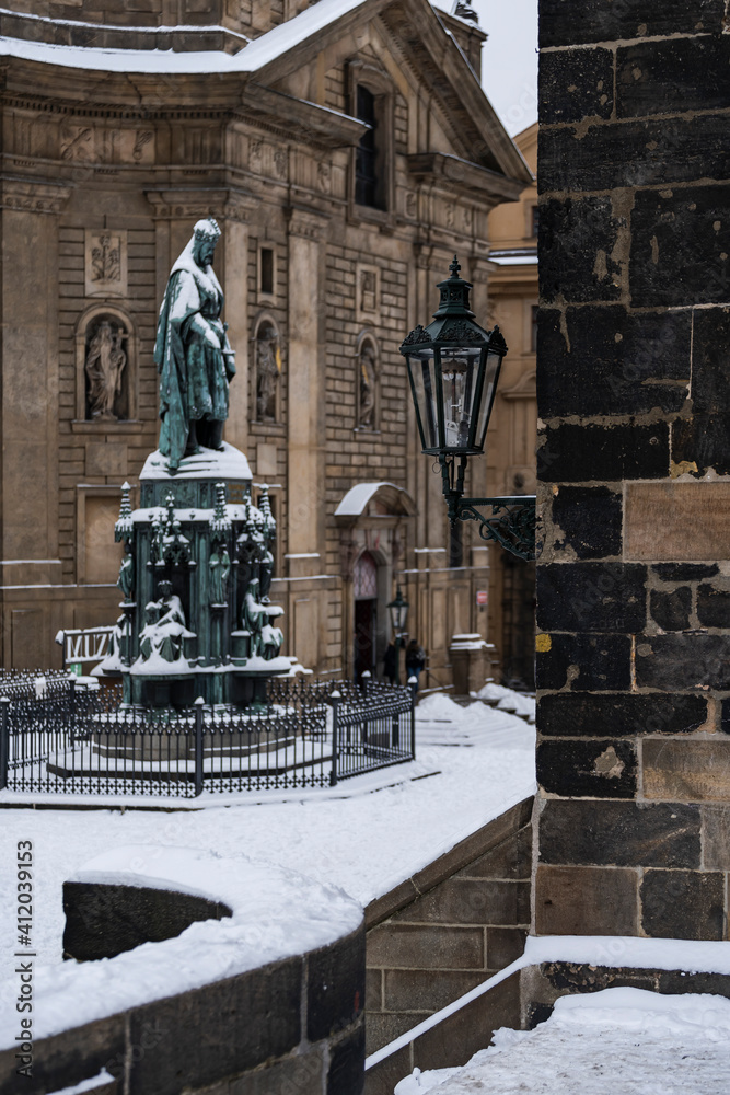 Fototapeta premium street light lamp on Charles Bridge and in the background a snow-covered statue of the monument to Charles 4 from the 18th century in Prague