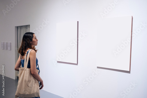 Young woman walking through a gallery and looking at the canvas.