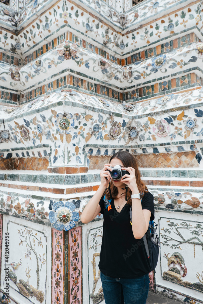 Young asian backpacker woman in black shirt taking picture at wat arun.