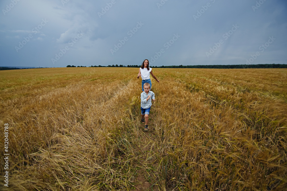 A happy family of mother and son in a summer wheat field. The boy runs merrily across the field. Rural landscape.