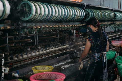 Female worker stands processing silk worms in a silk factory.