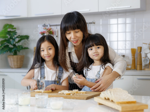 Beautiful and cute Asian mother teaching and showing the 2 daughters, 3 years and 7 years old, how to cut and slice bread