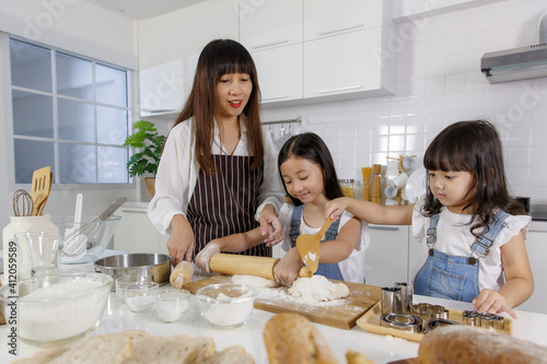 Beautiful Asian mother teaching two young daughters how to make a bakery in a modern kitchen. Idea for love and relationship of a family at home.