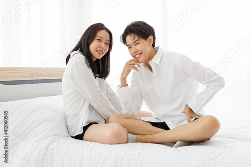 LGBTQ couple lovers, a handsome girl as man or butch and femme, spending and sharing loving time in white bedroom with fun, warmth, and happiness