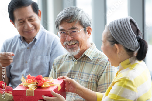 Senior Asian people joining together and give the gift boxes to each other and the man feels excited. Concept for happy lifestyle and good relationship with older people