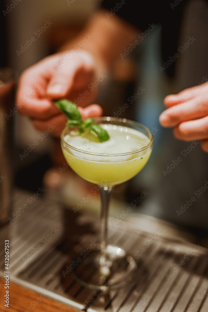 Bartender garnishing sour cocktail in a coupe glass with a basil leaf. Lifestyle vertical image. Selective focus. Bartender garnishing sour cocktail in a coupe glass with a basil leaf. Lifestyle vertical image. Selective focus.