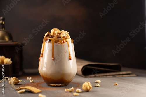 Fototapeta Sweet Milkshake with caramel syrup,cream liqueur,caramel popcorn and chocolate powder on brown background with vintage,manual coffee grinder