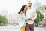 Beautiful young Chinese woman in love hugging boyfriend when they are standing on city square