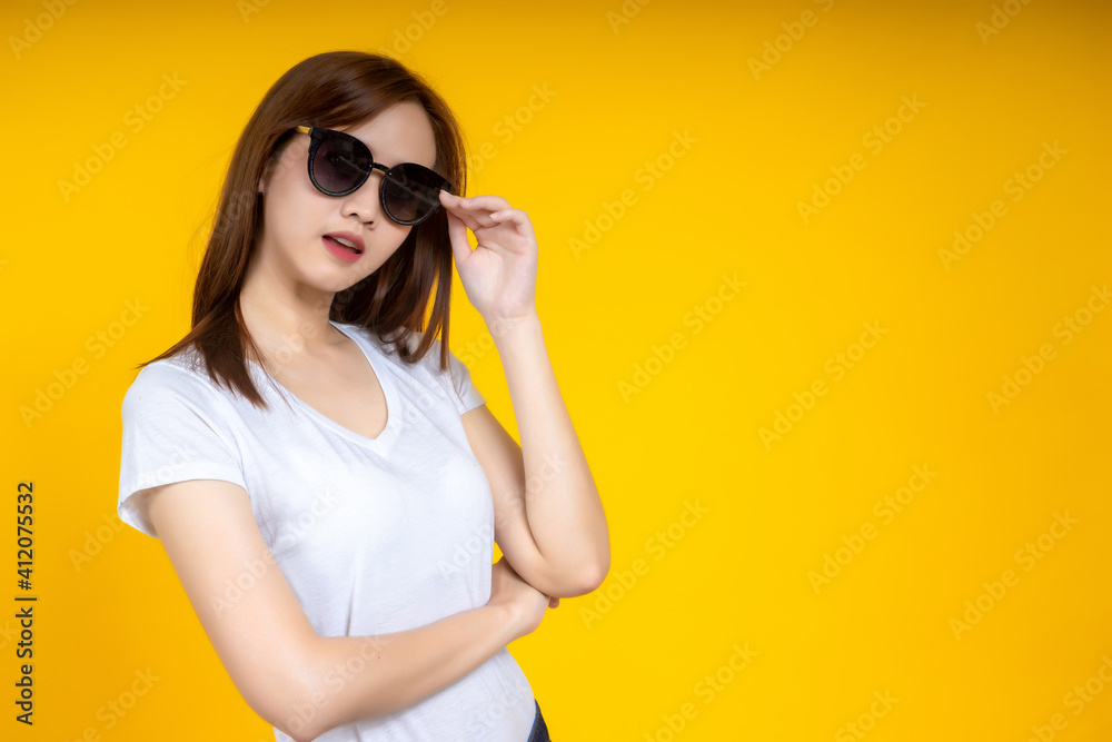 Young Asian woman in white casual t-shirt looking aside, wearing sunglass isolated on bright yellow wall background in studio. People lifestyle concept. Mock up copy space Young Asian woman in white casual t-shirt looking aside, wearing sunglass isolated on bright yellow wall background in studio. People lifestyle concept. Mock up copy space