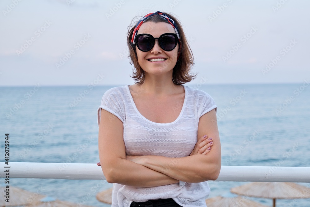 Smiling mature woman in sunglasses looking at camera with crossed arms
