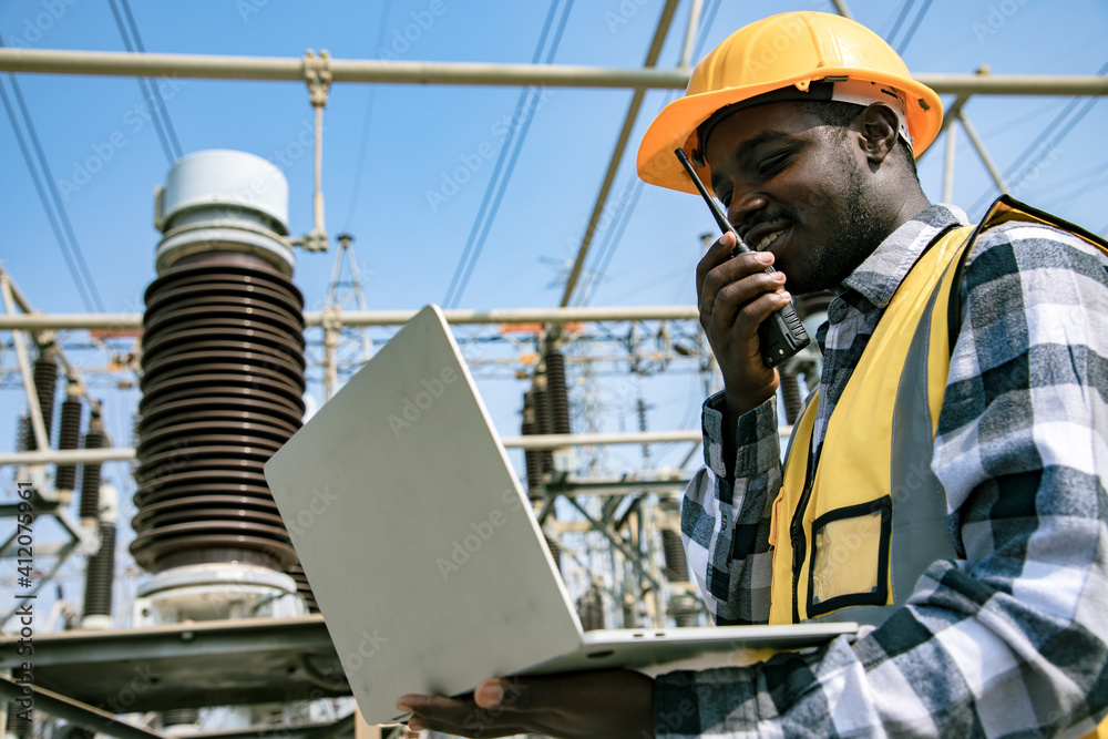 Handsome engineering man holding paper projects plan and using walkie talkie in front of High power power plant. Back view of contractor on background of power plant buildings. Handsome engineering man holding paper projects plan and using walkie talkie in front of High power power plant. Back view of contractor on background of power plant buildings.