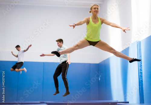 Young athletic woman practicing side split in jump on trampoline in sports center..