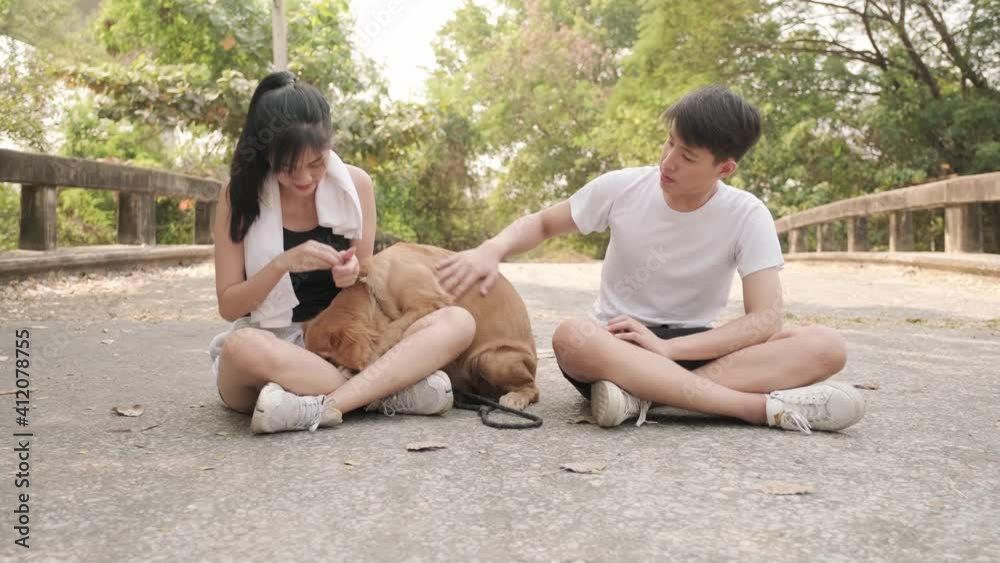 Young Asian couple playing with a golden retriever dog and smiling together after jogging at outdoor park on evening. Young Asian couple playing with a golden retriever dog and smiling together after jogging at outdoor park on evening.