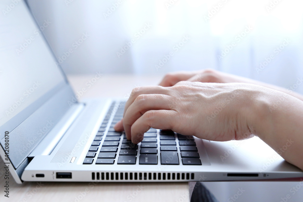 Female hands on laptop keyboard on a desk in sunlight. Woman types on the laptop keyboard sitting near the window, office or home work Female hands on laptop keyboard on a desk in sunlight. Woman types on the laptop keyboard sitting near the window, office or home work
