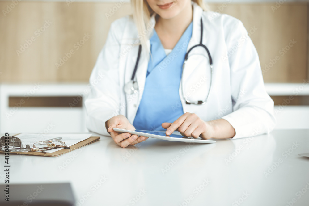Unknown woman-doctor standing in clinic and using tablet pc, close-up. Data and best service in medicine and healthcare Unknown woman-doctor standing in clinic and using tablet pc, close-up. Data and best service in medicine and healthcare