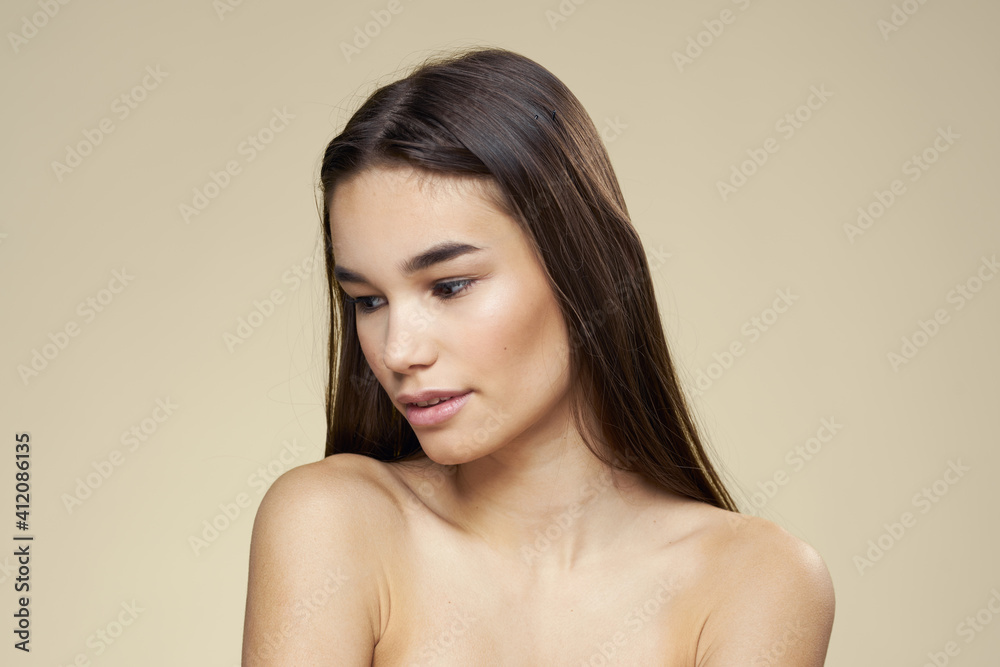 Woman with bared shoulders dark hair clean skin makeup beige background Woman with bared shoulders dark hair clean skin makeup beige background