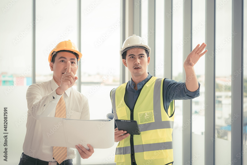Professional two engineers are discussing the new project. The senior man is standing and holding the blueprint. Professional two engineers are discussing the new project. The senior man is standing and holding the blueprint.