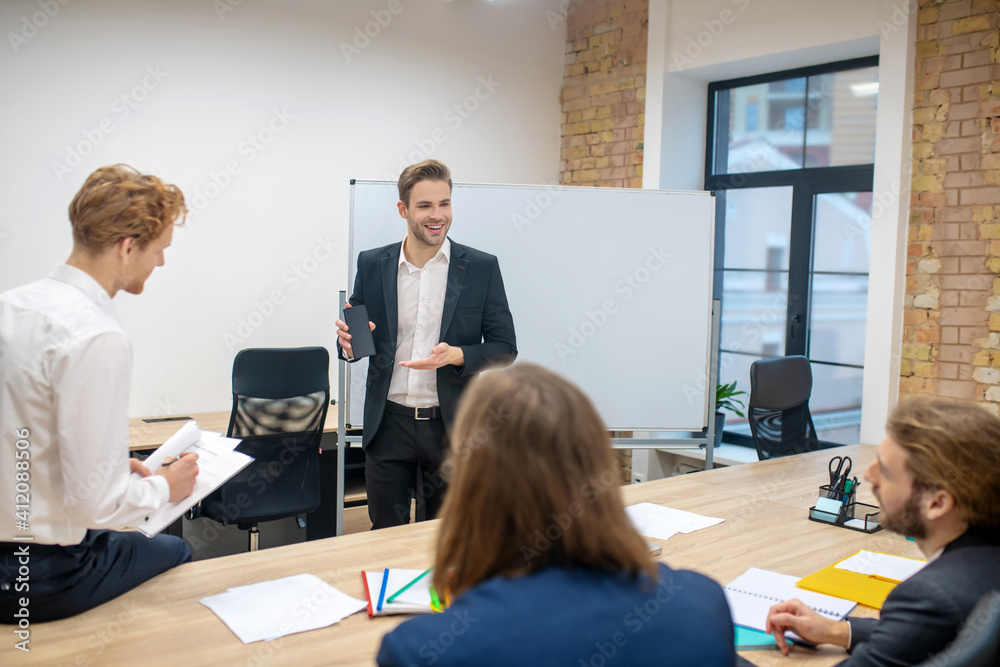 © zinkevych - Smiling man showing smartphone and interested colleagues