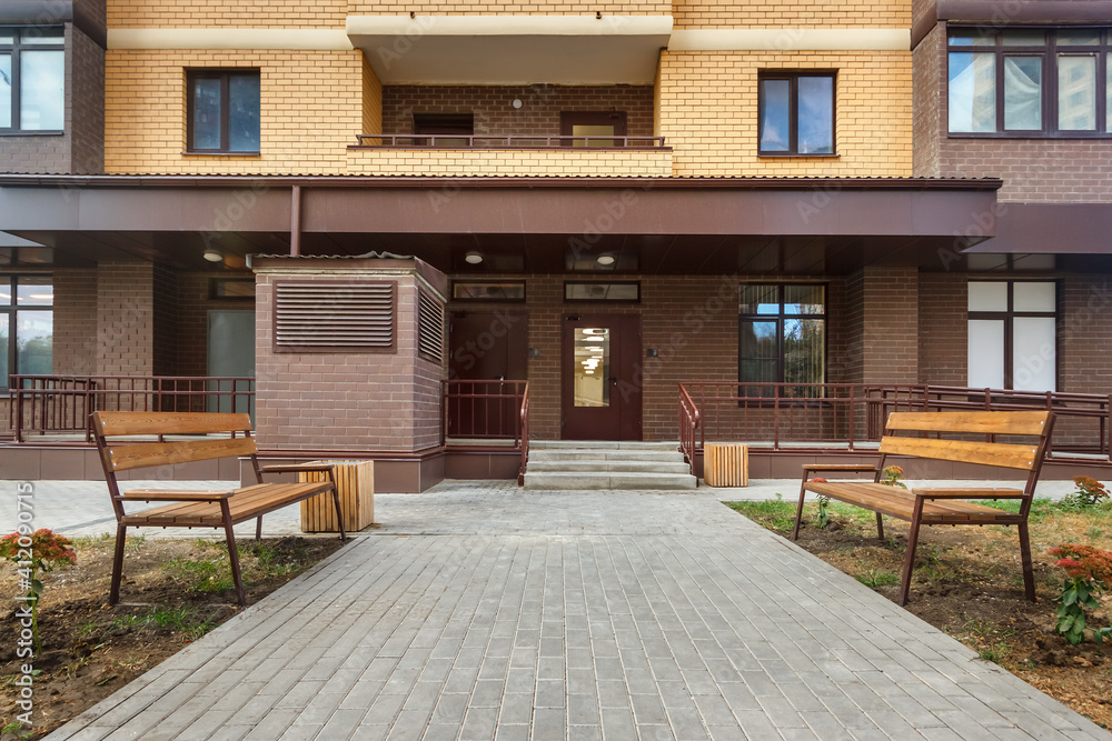 Entrance in new modern high-rise residential building with paving stone walkway and benches on both sides