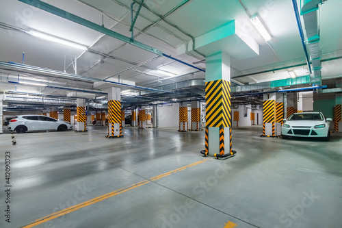 Inside view of bright and clean underground parking garage with cars in basement of high-rise apartment building