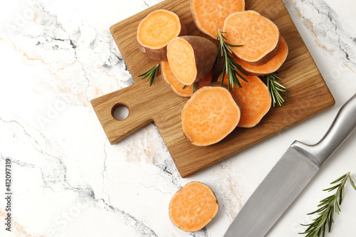 Composition of Fresh ripe sweet potatoes and rosemary spice on table against marble background