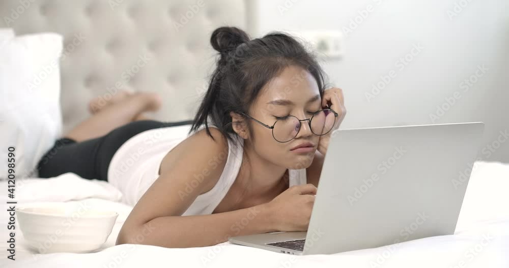 Young beautiful glasses asian woman lying in white bedroom. Girl take a nap while using laptop computer. Sleepy lady in casual clothes at house during quarantine. Social distance new normal concept. Young beautiful glasses asian woman lying in white bedroom. Girl take a nap while using laptop computer. Sleepy lady in casual clothes at house during quarantine. Social distance new normal concept.