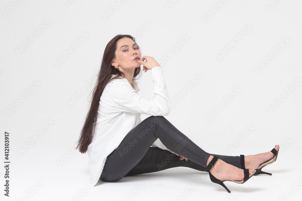 A beautiful girl of 25, European appearance, with dark long hair, in a white shirt and black trousers, sits in a light studio and looks languidly. Pleasure, relaxation A beautiful girl of 25, European appearance, with dark long hair, in a white shirt and black trousers, sits in a light studio and looks languidly. Pleasure, relaxation