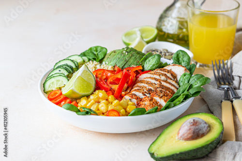 Healthy buddha bowl lunch with grilled chicken and bulgur, spinach, avocado, cucumber, bell pepper and corn on light background. Delicious balanced food concept.