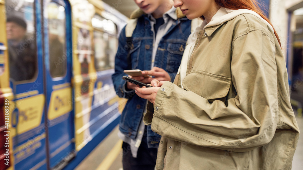 Cropped shot of young people using smartphones at the subway metro station. Couple of teenagers using mobile app, checking public transport schedule