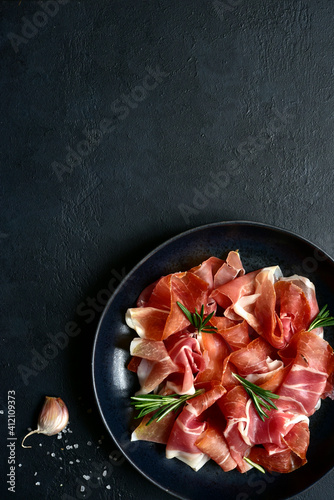 Slices of prosciutto di parma or jamon serrano (iberico)  on a black plate. Top view with copy space.