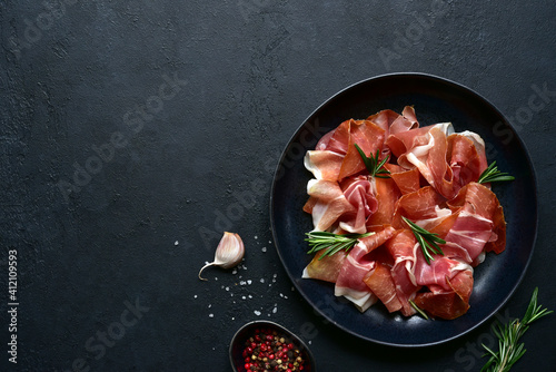 Slices of prosciutto di parma or jamon serrano (iberico) on a black plate. Top view with copy space.