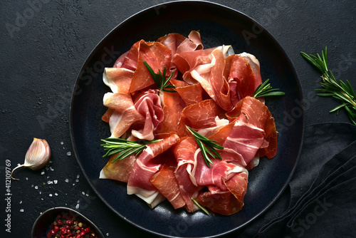 Photos Slices of prosciutto di parma or jamon serrano (iberico)  on a black plate
