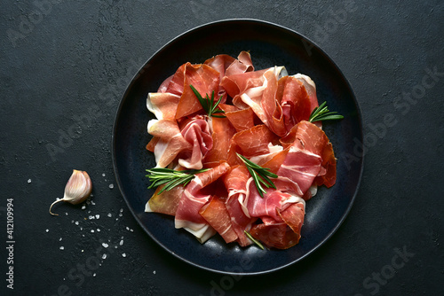 Slices of prosciutto di parma or jamon serrano (iberico)  on a black plate. Top view with copy space. photo