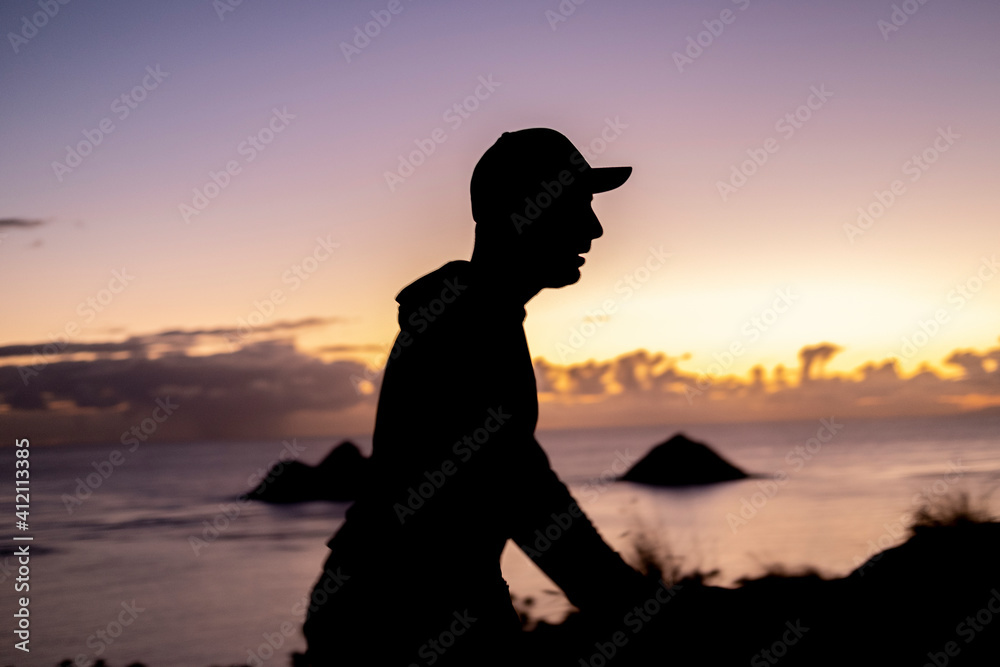 Silhouette of a man hiking on a mountain top overlooking two islands in the ocean.