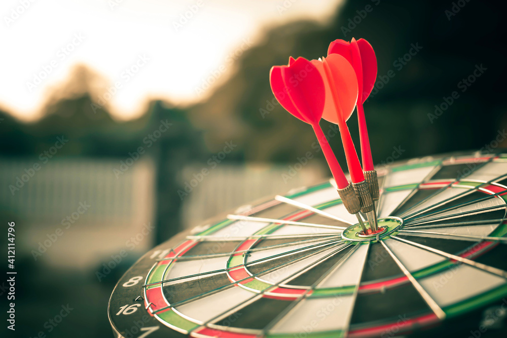 Fototapeta premium Close up shot of the dart arrow hit on bulleyes of dartboard to represent that the business reached the target with dark tone picture style. Target and goal as concept.